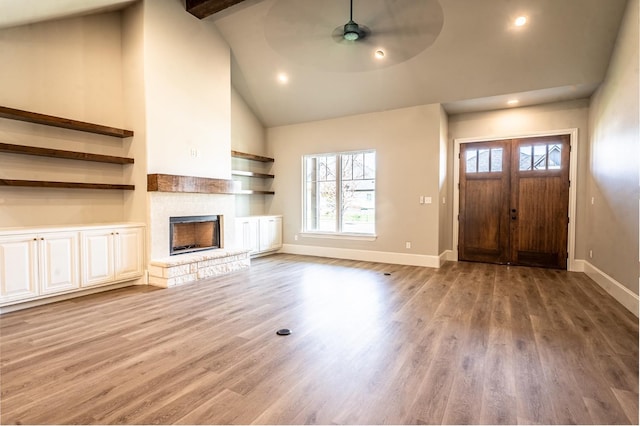 unfurnished living room with a stone fireplace, hardwood / wood-style floors, high vaulted ceiling, ceiling fan, and beam ceiling