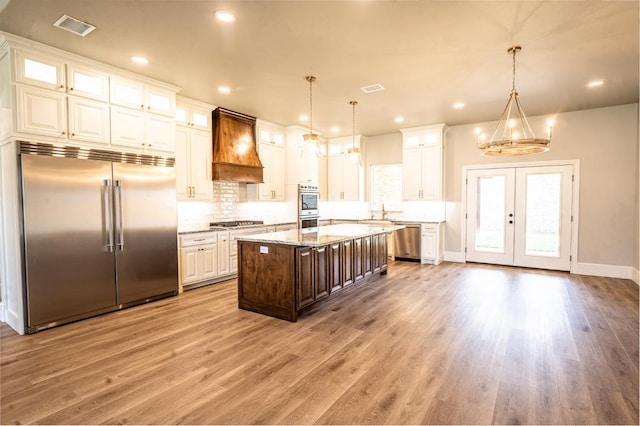 kitchen with custom exhaust hood, light stone counters, decorative light fixtures, appliances with stainless steel finishes, and a kitchen island