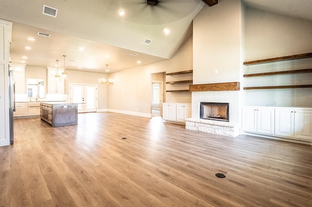 unfurnished living room with sink, light hardwood / wood-style flooring, high vaulted ceiling, a notable chandelier, and a fireplace