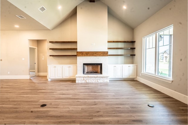 unfurnished living room featuring a stone fireplace, high vaulted ceiling, and light hardwood / wood-style floors