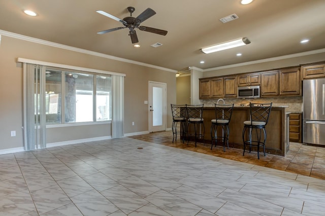 kitchen with ornamental molding, appliances with stainless steel finishes, a breakfast bar, and decorative backsplash