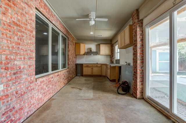 kitchen featuring brick wall, light brown cabinetry, sink, ceiling fan, and wall chimney range hood