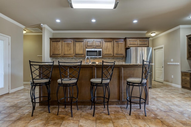 kitchen featuring a kitchen island with sink, crown molding, a breakfast bar area, and stainless steel appliances