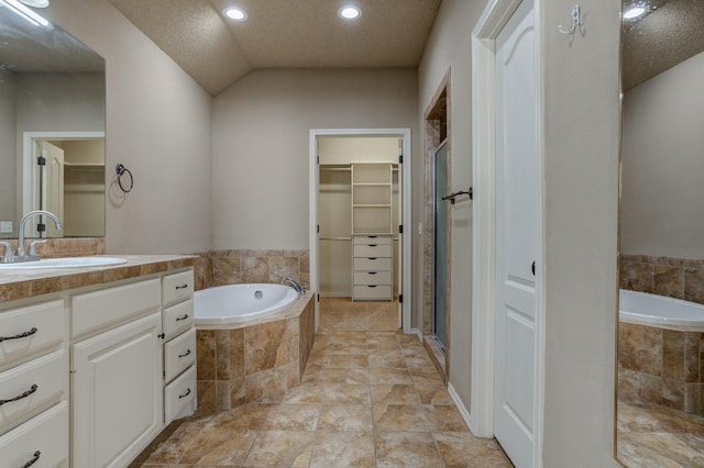 bathroom featuring independent shower and bath, vanity, lofted ceiling, and a textured ceiling