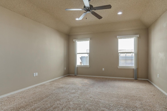 carpeted spare room with ceiling fan, vaulted ceiling, a textured ceiling, and plenty of natural light