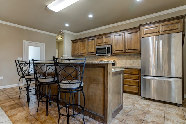 kitchen featuring appliances with stainless steel finishes, an island with sink, a kitchen breakfast bar, ornamental molding, and light stone counters