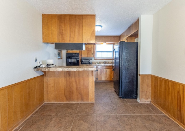 kitchen with black appliances, sink, a breakfast bar area, kitchen peninsula, and a textured ceiling