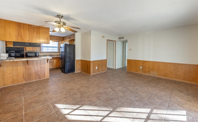 kitchen featuring a textured ceiling, wooden walls, kitchen peninsula, ceiling fan, and black appliances