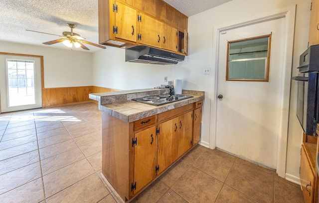 kitchen featuring black oven, wood walls, ceiling fan, gas stovetop, and a textured ceiling