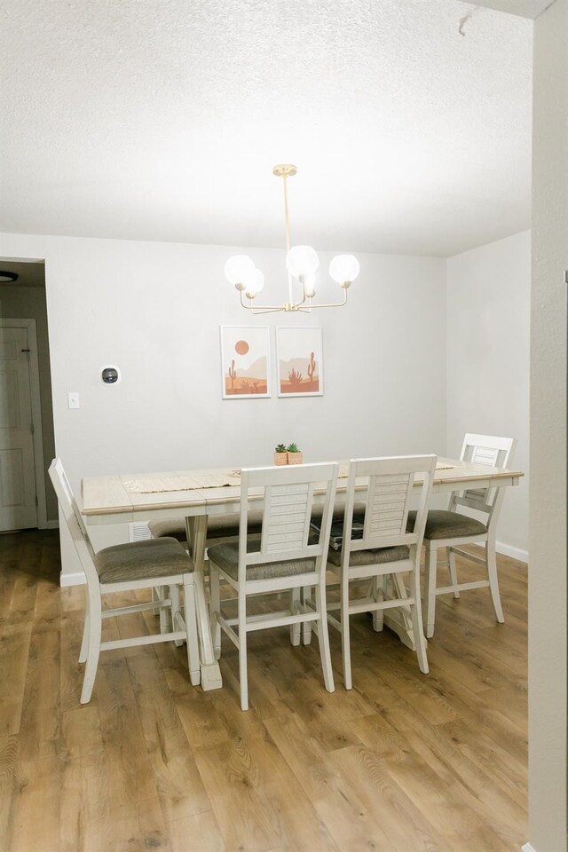 dining room featuring a textured ceiling, a notable chandelier, and light wood-type flooring