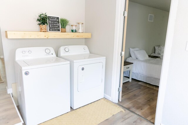 laundry room with washing machine and clothes dryer and light hardwood / wood-style flooring