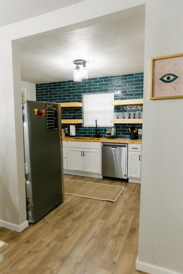 kitchen featuring butcher block countertops, white cabinetry, stainless steel appliances, tasteful backsplash, and light wood-type flooring