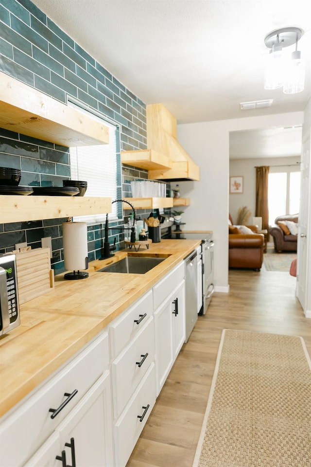 kitchen with sink, light hardwood / wood-style flooring, wooden counters, backsplash, and white cabinets