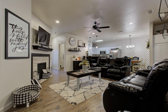 living room with light wood-style flooring, an accent wall, ceiling fan with notable chandelier, a fireplace, and recessed lighting