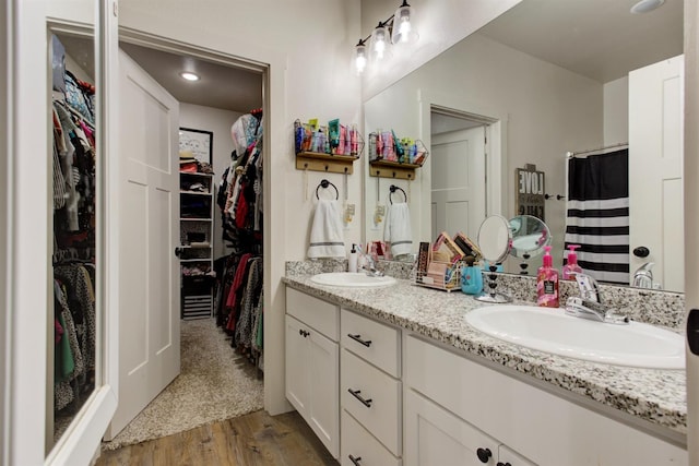 full bathroom with double vanity, a spacious closet, a sink, and wood finished floors