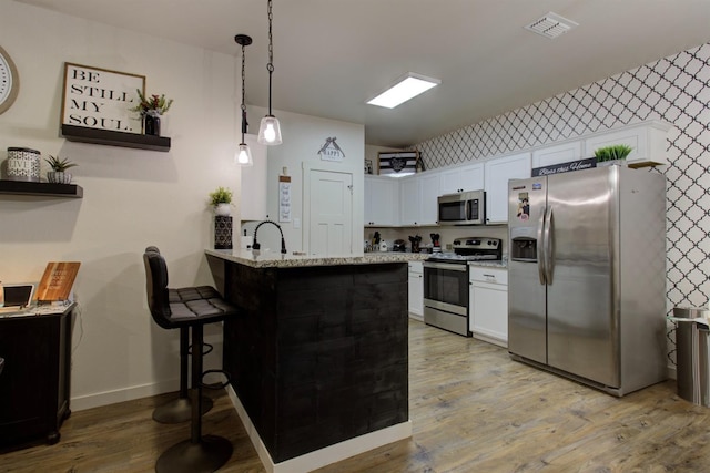 kitchen with appliances with stainless steel finishes, visible vents, white cabinets, and a peninsula