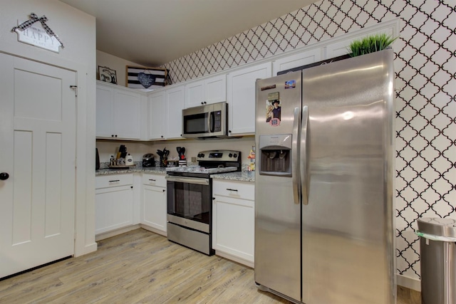 kitchen featuring light stone counters, stainless steel appliances, white cabinetry, light wood-type flooring, and wallpapered walls