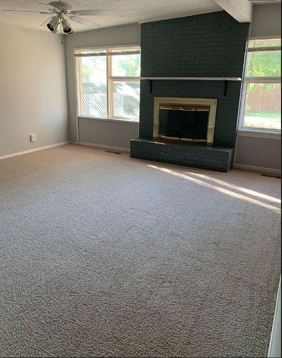 unfurnished living room featuring ceiling fan, a fireplace, a textured ceiling, and carpet flooring