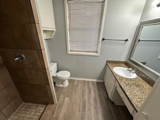 bathroom featuring vanity, tiled shower, hardwood / wood-style floors, and toilet