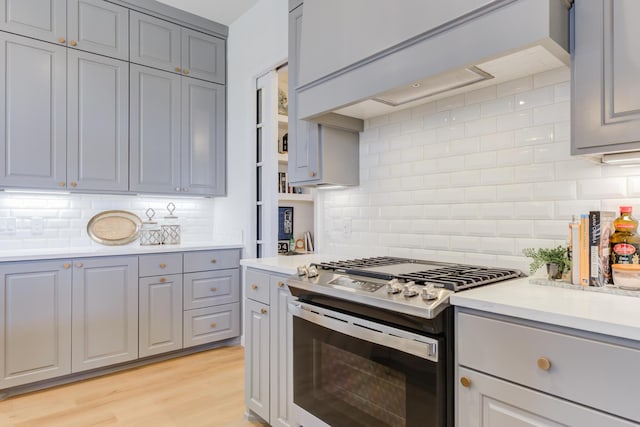 kitchen with tasteful backsplash, stainless steel range with gas cooktop, gray cabinets, and light wood-type flooring