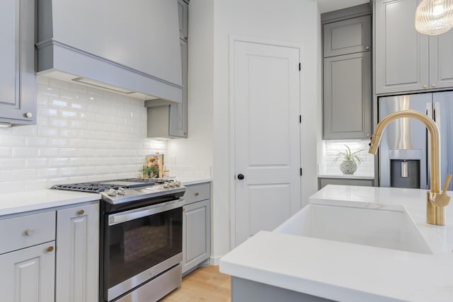 kitchen featuring backsplash, stainless steel appliances, custom range hood, and gray cabinetry