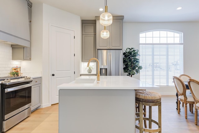 kitchen with sink, light wood-type flooring, appliances with stainless steel finishes, gray cabinets, and an island with sink