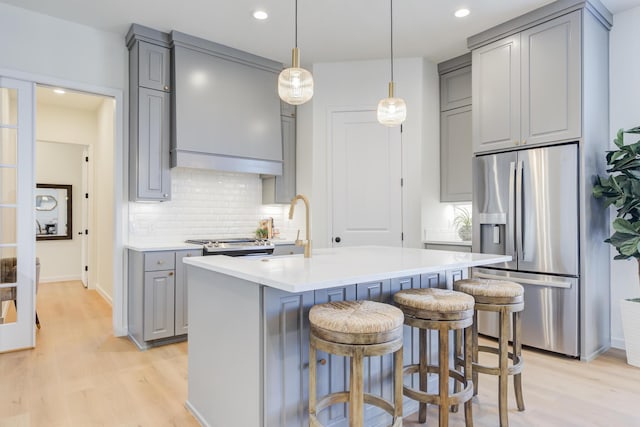 kitchen featuring gray cabinets, appliances with stainless steel finishes, an island with sink, sink, and a kitchen bar