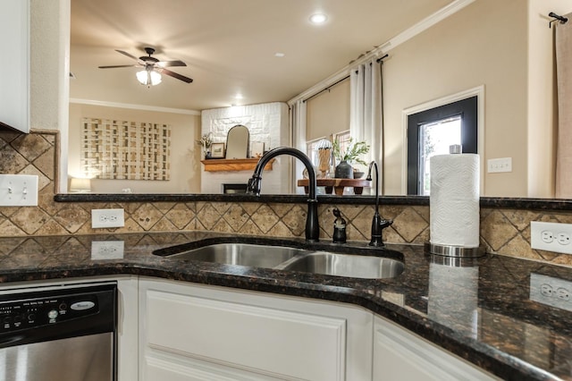 kitchen with sink, stainless steel dishwasher, ornamental molding, dark stone counters, and white cabinets