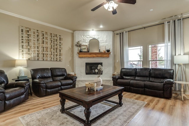 living room with crown molding, a fireplace, ceiling fan, and light wood-type flooring