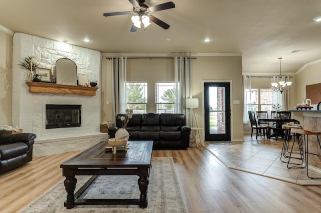 living room with ornamental molding, ceiling fan with notable chandelier, hardwood / wood-style floors, and a fireplace