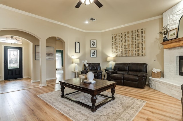 living room featuring crown molding, ceiling fan, a fireplace, and light wood-type flooring