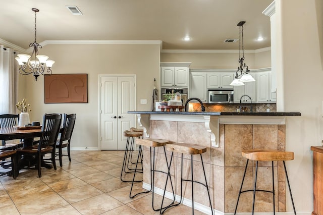 kitchen with hanging light fixtures, ornamental molding, white cabinets, and backsplash