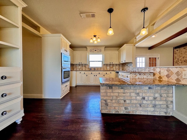 kitchen featuring light stone counters, dark hardwood / wood-style flooring, kitchen peninsula, stainless steel appliances, and backsplash