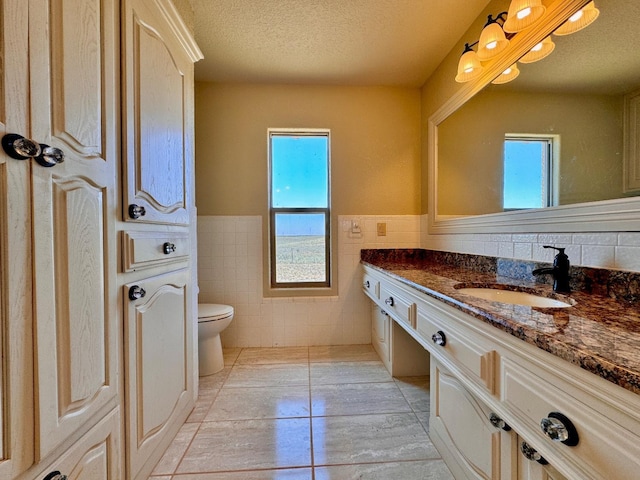 bathroom with tile patterned floors, toilet, a textured ceiling, tile walls, and vanity