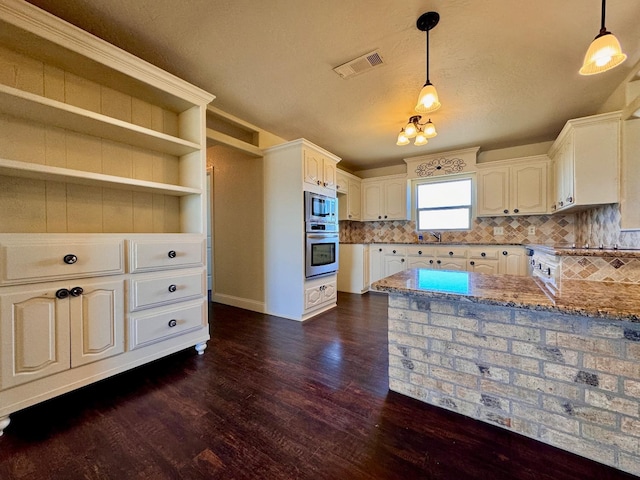 kitchen featuring pendant lighting, dark wood-type flooring, appliances with stainless steel finishes, tasteful backsplash, and light stone countertops