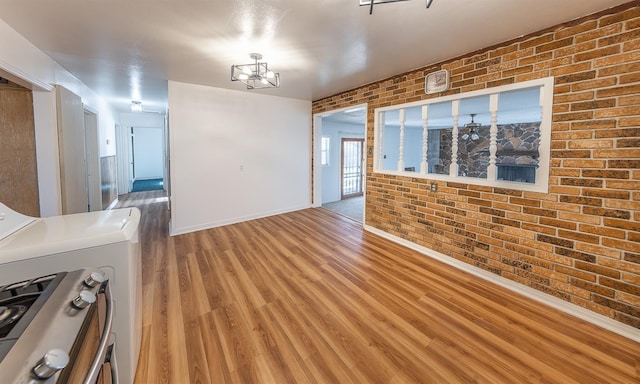 unfurnished living room featuring hardwood / wood-style flooring, brick wall, and washer / dryer