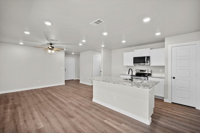 kitchen featuring white cabinetry, appliances with stainless steel finishes, light stone countertops, and a kitchen island with sink