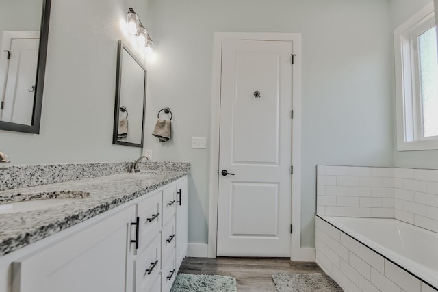 bathroom with vanity, tiled tub, and hardwood / wood-style floors