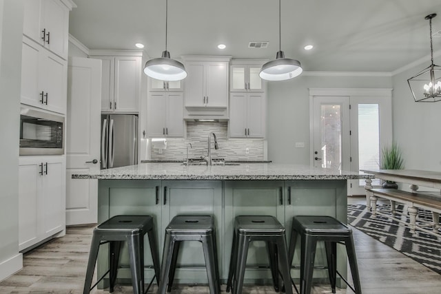 kitchen with built in microwave, sink, decorative light fixtures, stainless steel refrigerator, and a kitchen island with sink