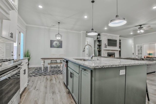 kitchen featuring sink, stainless steel range with electric cooktop, white cabinetry, decorative light fixtures, and a center island with sink