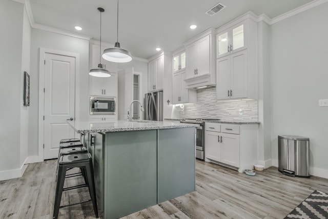 kitchen featuring a center island with sink, light stone countertops, white cabinets, and appliances with stainless steel finishes