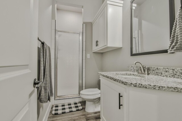 bathroom featuring vanity, hardwood / wood-style floors, a shower with shower door, and toilet