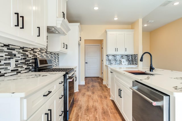 kitchen featuring appliances with stainless steel finishes, white cabinetry, sink, decorative backsplash, and light wood-type flooring