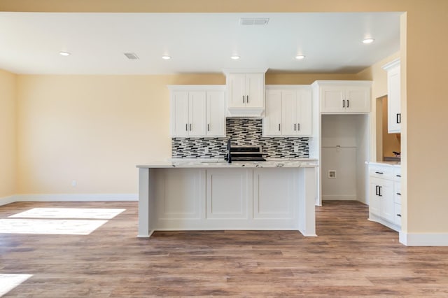 kitchen featuring a kitchen island with sink, backsplash, white cabinets, and light wood-type flooring