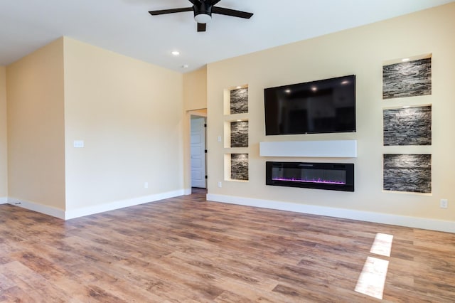 unfurnished living room with ceiling fan, wood-type flooring, and built in features