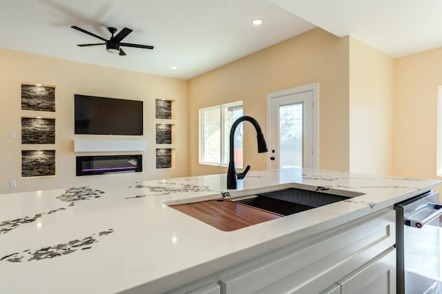 kitchen with light stone counters, ceiling fan, and sink