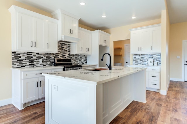 kitchen featuring white cabinetry, an island with sink, sink, stainless steel range, and light stone countertops