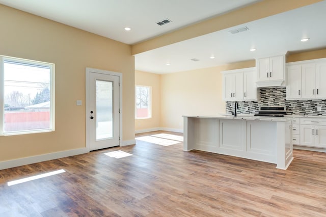 kitchen featuring stainless steel electric range oven, tasteful backsplash, white cabinetry, a kitchen island with sink, and light wood-type flooring