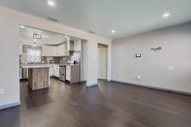 kitchen featuring appliances with stainless steel finishes, dark hardwood / wood-style floors, tasteful backsplash, a kitchen island, and wall chimney exhaust hood