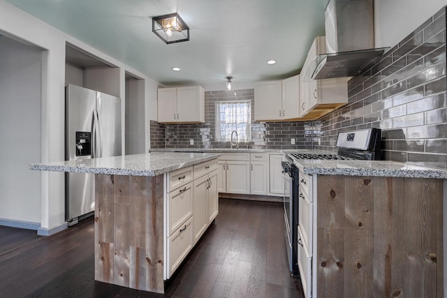 kitchen with white cabinetry, appliances with stainless steel finishes, a kitchen island, light stone countertops, and wall chimney range hood